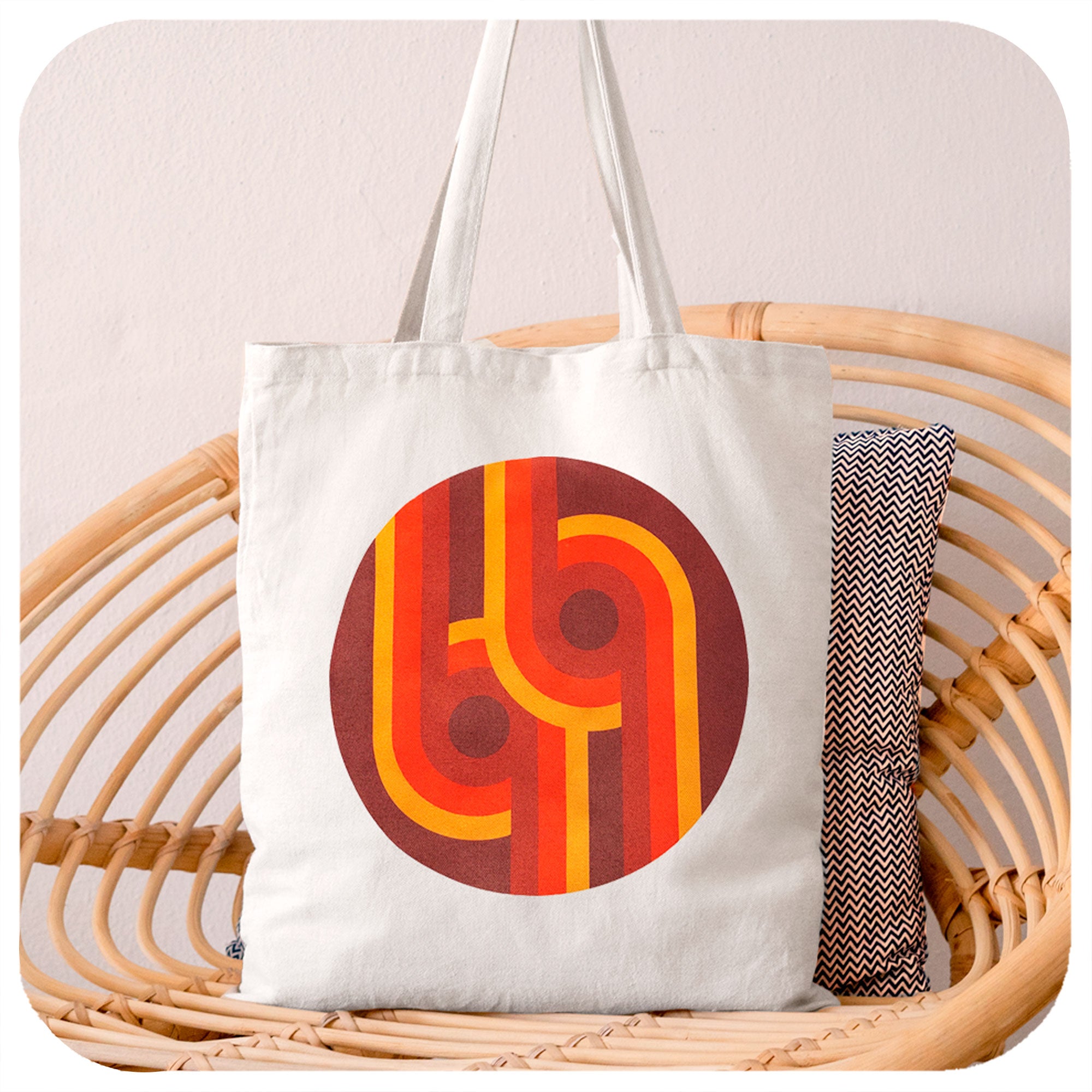 A canvas style tote bag featuring a 70s supergaphic print sits on a rattan chair | The Inkabilly Emporium