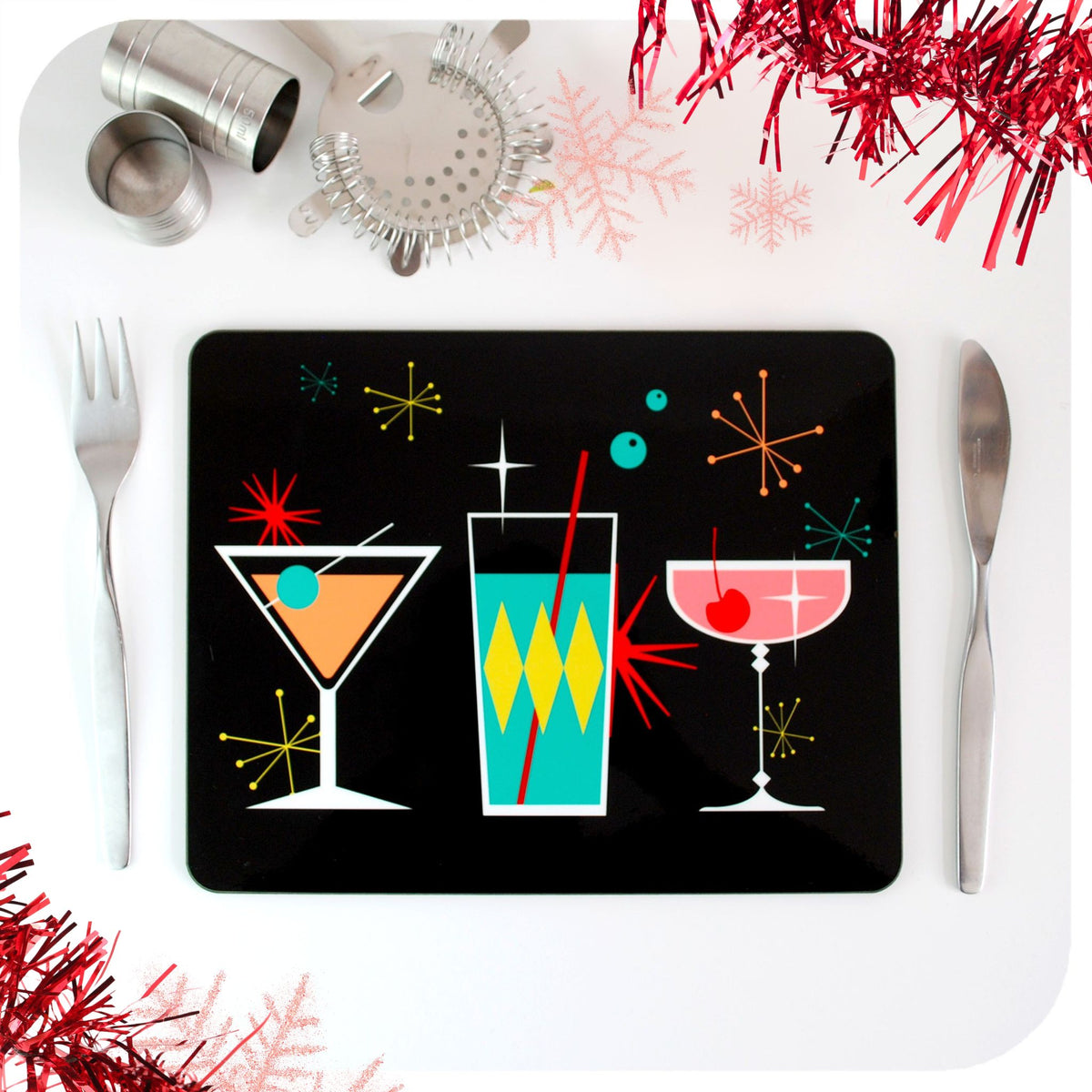 A placemat featuring mid century style cocktails site on a white table with cutlery, cocktail making equipment and red tinsel | The Inkabilly Emporium