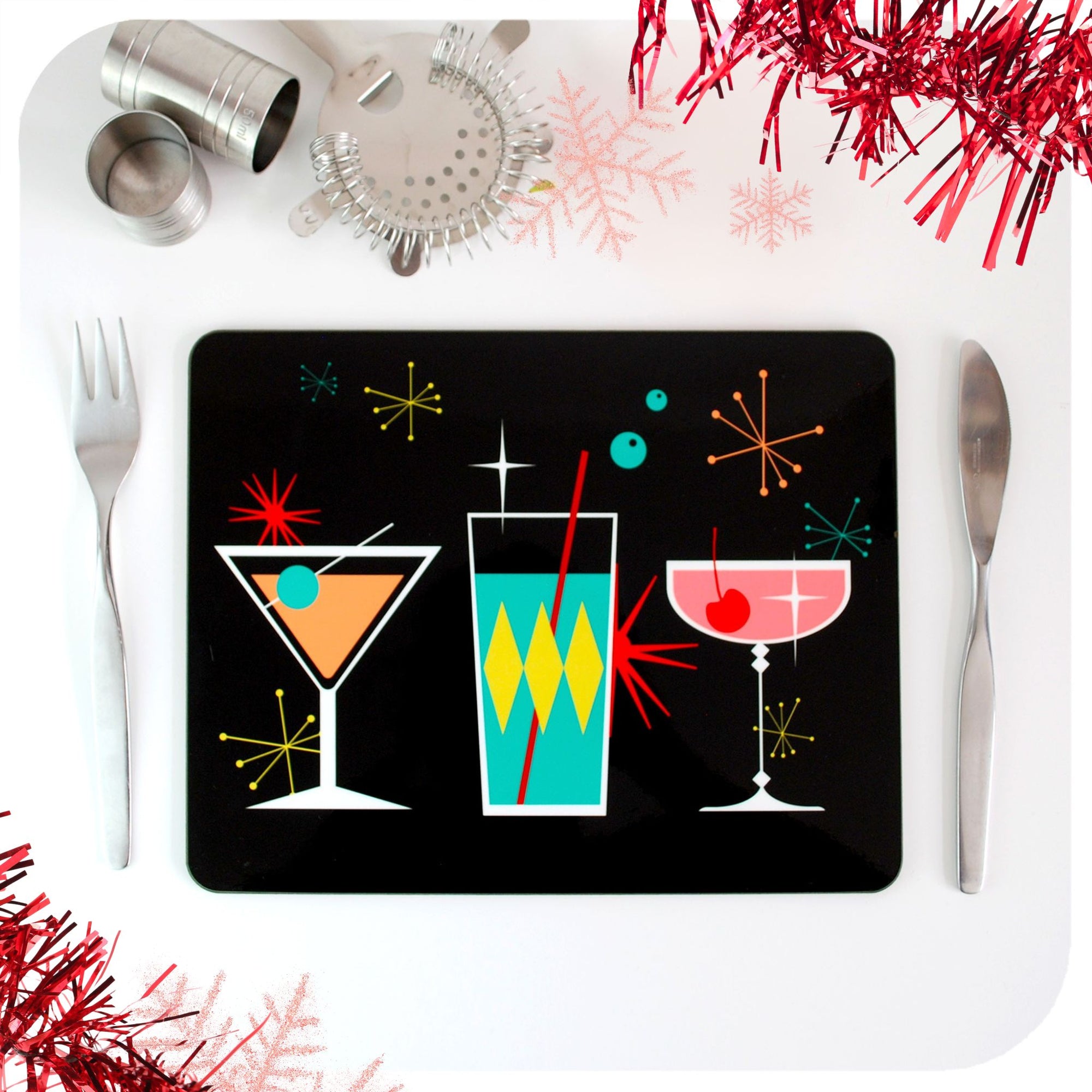 A placemat featuring mid century style cocktails site on a white table with cutlery, cocktail making equipment and red tinsel | The Inkabilly Emporium