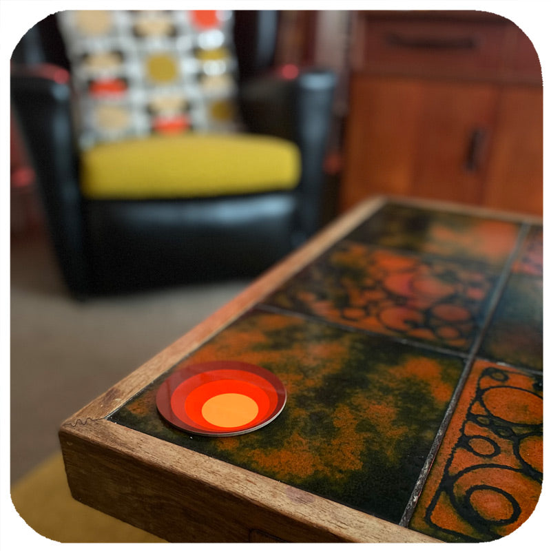 Customer photo of a single 70s style coaster on a vintage mid century coffee table in the foreground, blurred background features a Mid Century  armchairhair