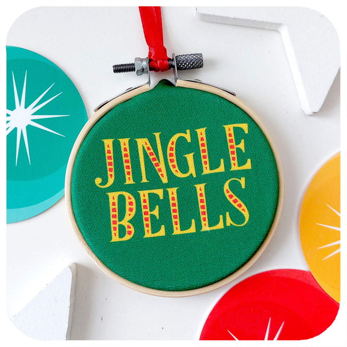 A printed fabric retro style Christmas tree decoration on a white background surrounded by colourful Christmas decorations. Text on bauble reads: Jingle Bells
