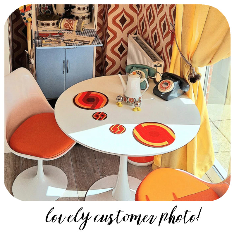 Round table with Inkabilly 70s Supergraphic tableware in a room with patterned curtains and colourful chairs.