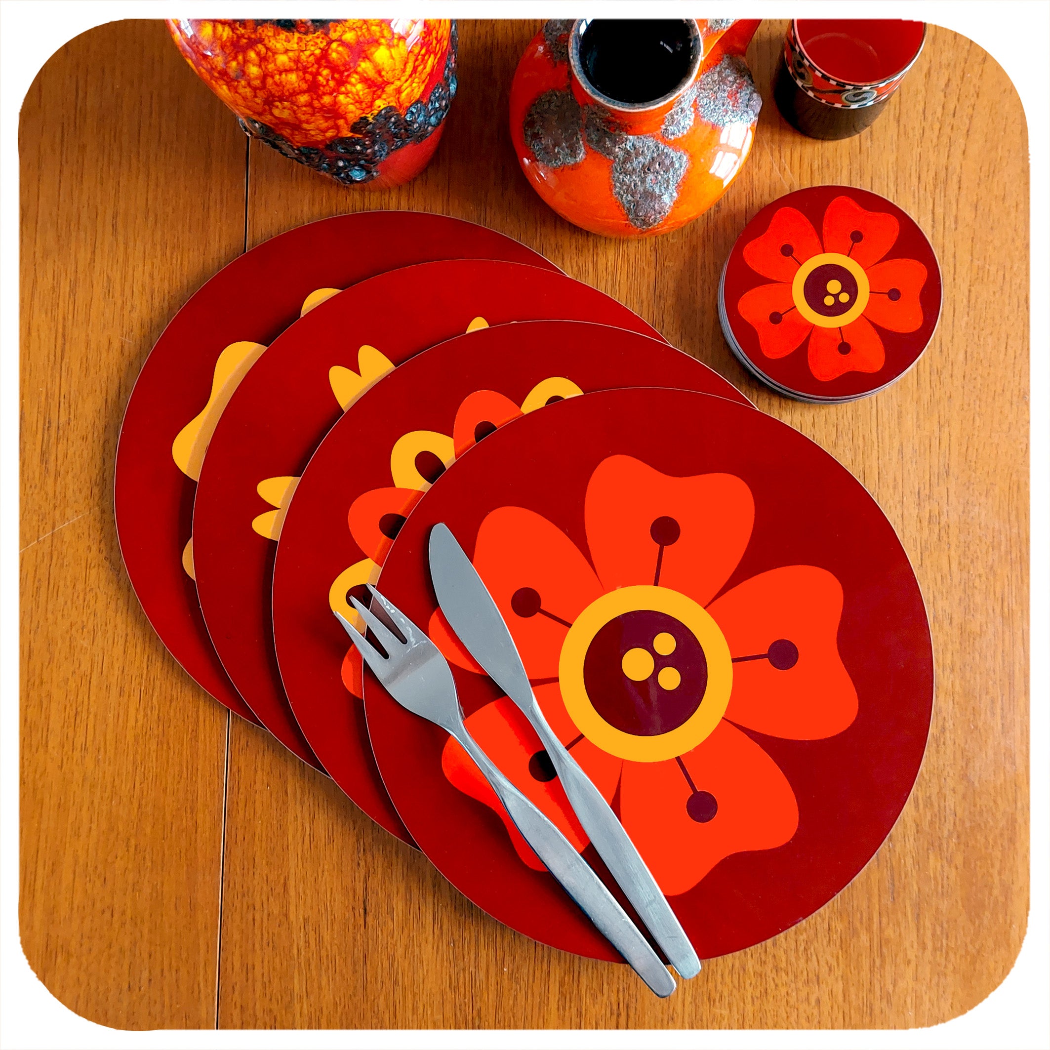 A set of four round 70s floral placemats  lie overlapped in a line on teak table with a set of matching coasters and  fat lava vases | The Inkabilly Emporium
