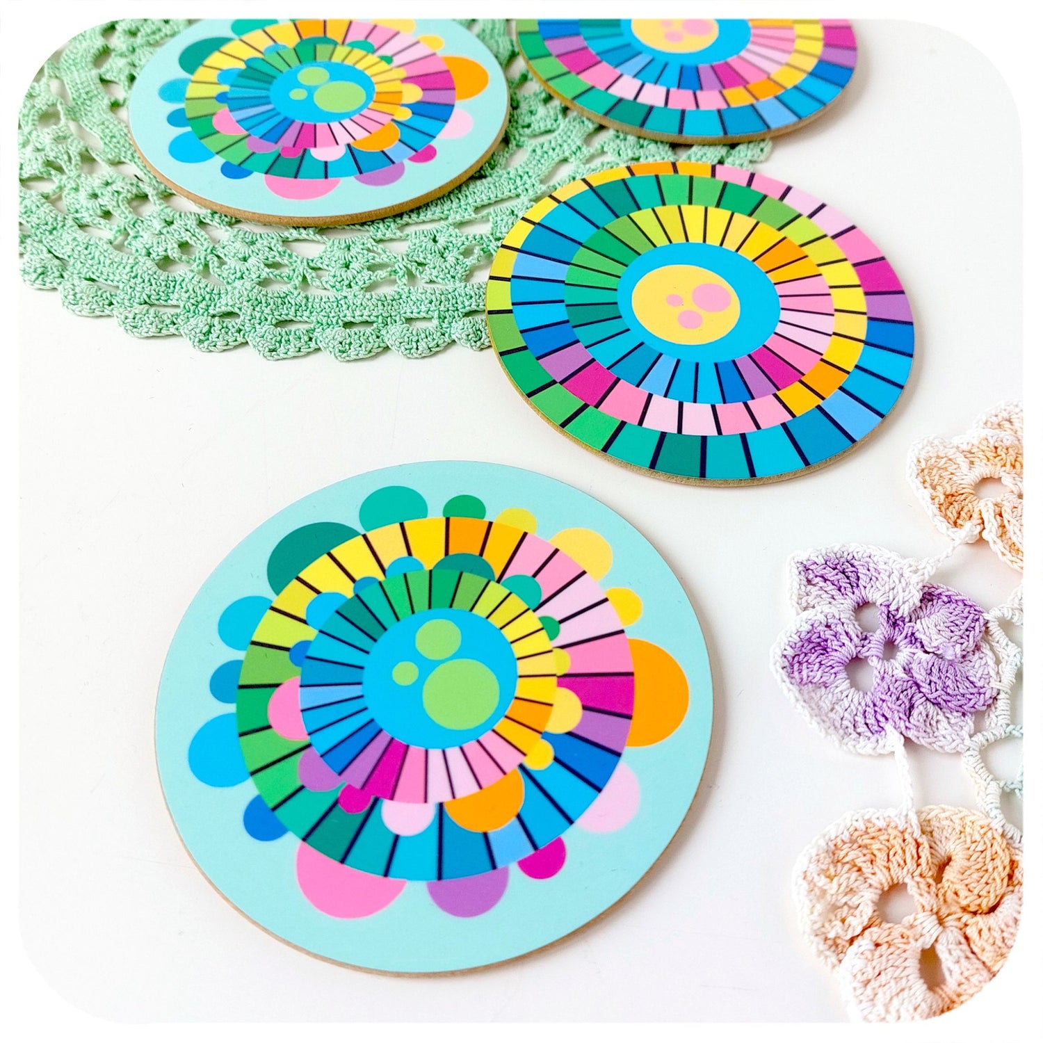 Set of four round coasters featuring multi-coloured abstract patterns lie scattered on a white table with vintage doilies | The Inkabilly Emporium