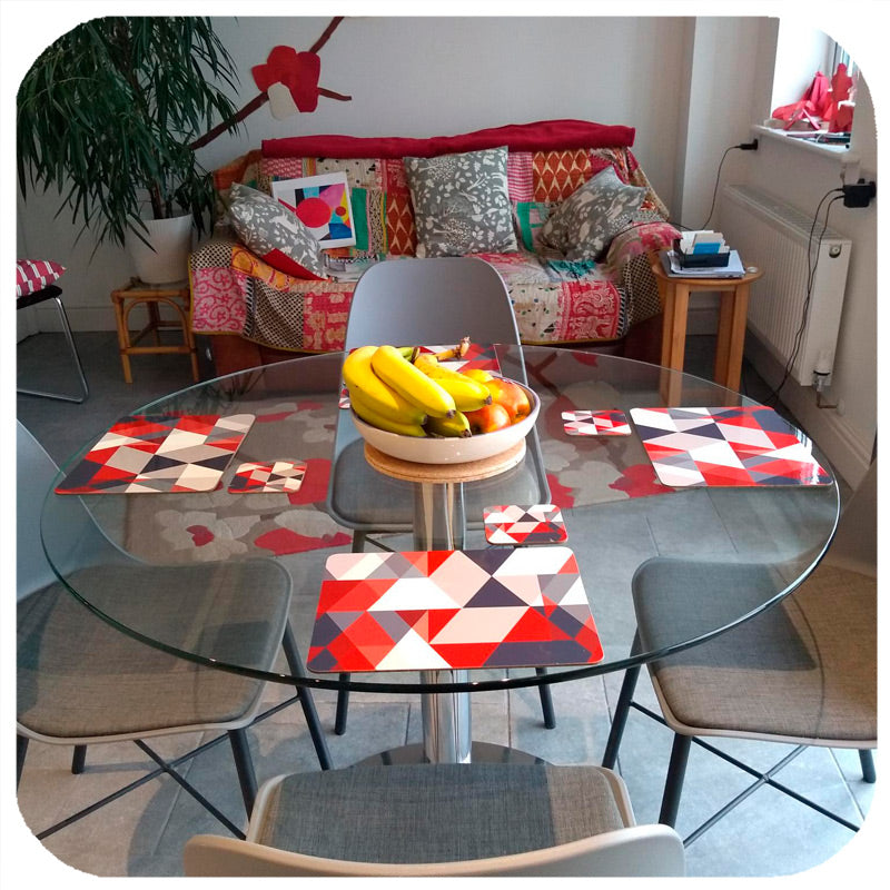 A round glass dining table is set with  Inkabilly's red & grey scandi geometric placemats and coasters, in a colourful rooms