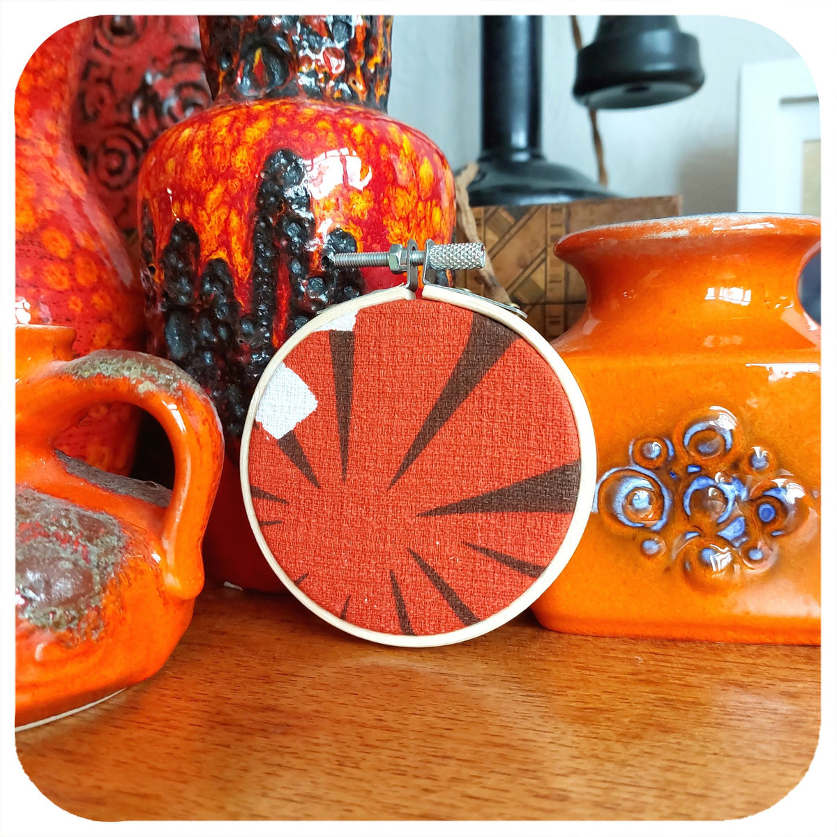 Vintage Fabric Embroidery Hoop sits with vintage orange pottery on a wooden surface