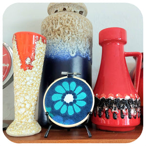 Embroidery hoop with floral design on a shelf with vintage fat lava vases