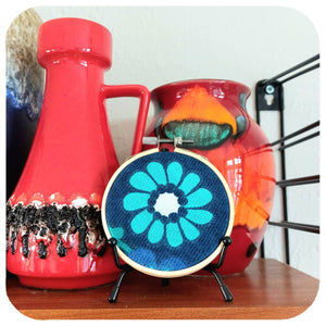 Embroidery hoop with floral design on a shelf with vintage vases