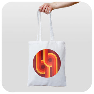 A canvas style tote bag featuring a 70s supergaphic print in orange, yellow, red and brown is being held against a white background | The Inkabilly Emporium