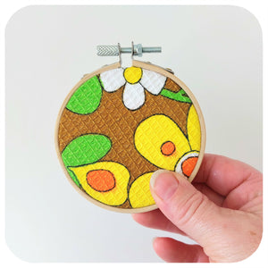 Hand holding a small embroidery hoop with a colourful floral design.