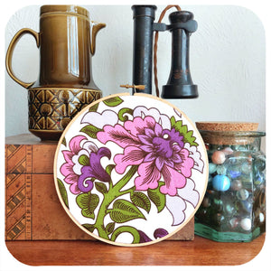 Decorative floral embroidery hoop on a wooden surface with vintage items.