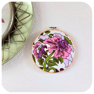 Floral embroidery hoop on a textured white wall with a green framed mirror 