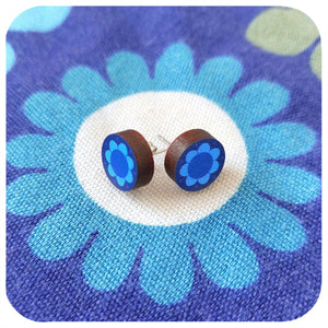 Blue flower-shaped wooden earrings on a blue fabric background