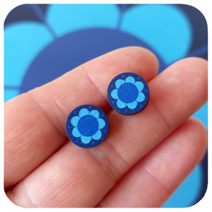 Blue floral stud earrings held between fingers with a blue background