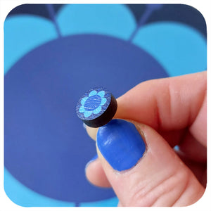 Hand holding a small blue stud earring with a blue background