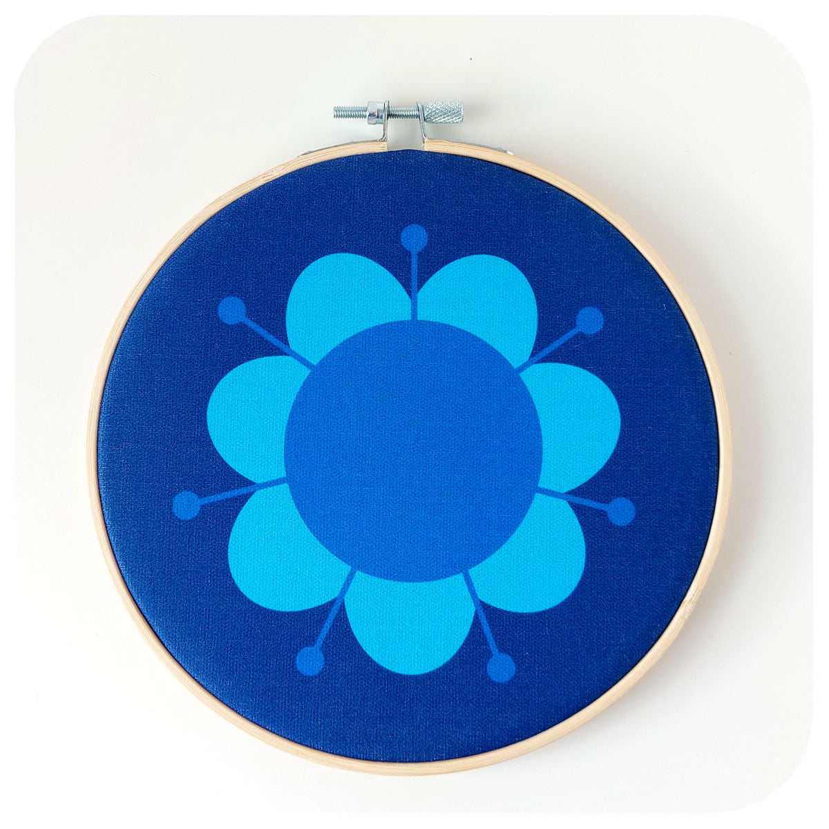 A round blue fabric wall art hoop featuring a hand-printed retro daisy design, framed in a bamboo embroidery hoop.