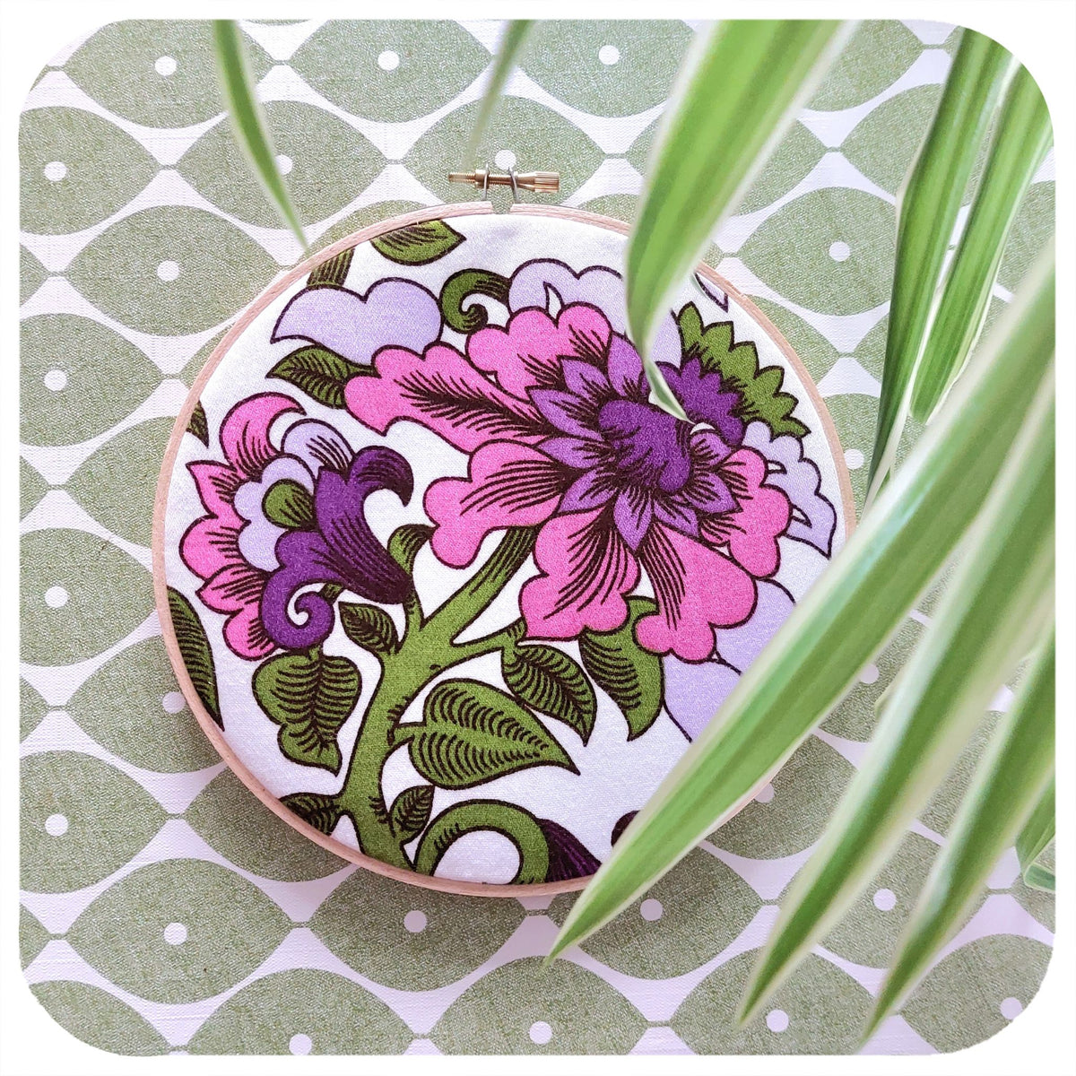 Embroidery hoop with floral design on a green and white patterned background