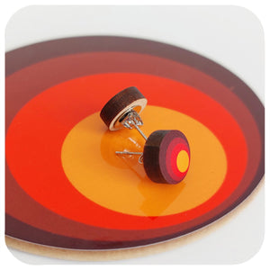 Wooden earrings on a circular coaster with concentric red, orange, and yellow rings.