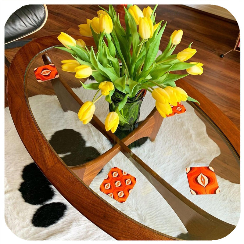Customer photo of 70s style orange op art coasters on a mid century glass table with a vase of yellow tulips,  on a cow hide rug a