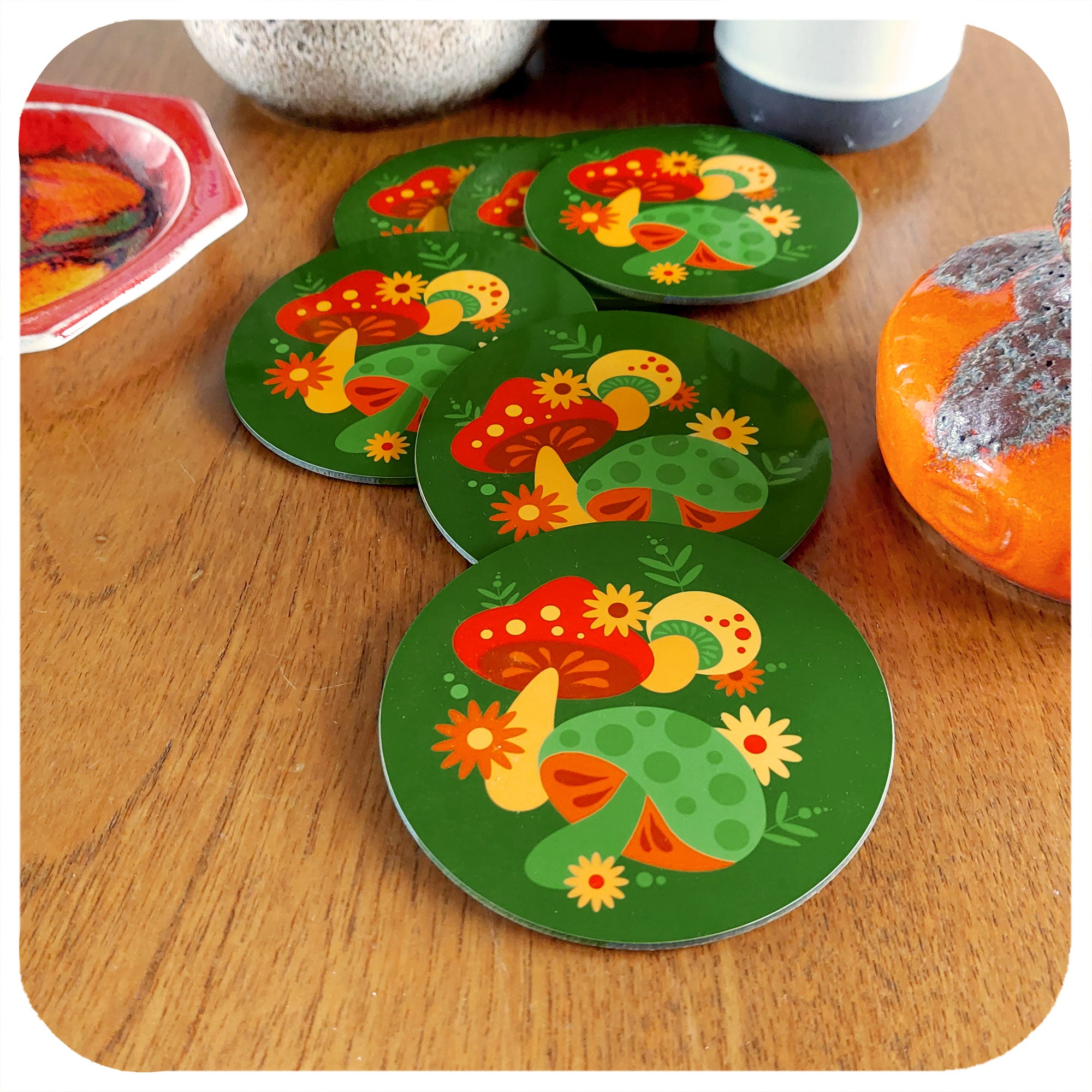 Set of 6 Round, Retro Mushrooms Coasters lie in a scattered pile with various vintage pottery pieces, on a teak table | The Inkabilly Emporium