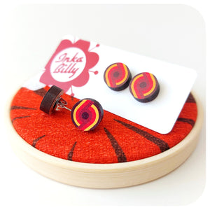 Red, yellow and brown spiral earrings on a red fabric with 'InkaBilly' branded backing card