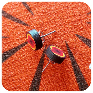 Round stud earrings with orange, red, and yellow design on an orange fabric background