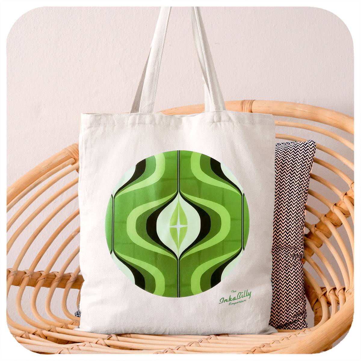 White Tote Bag featuring a green 70s style op art design sits on a rattan chair | The Inkabilly Emporium