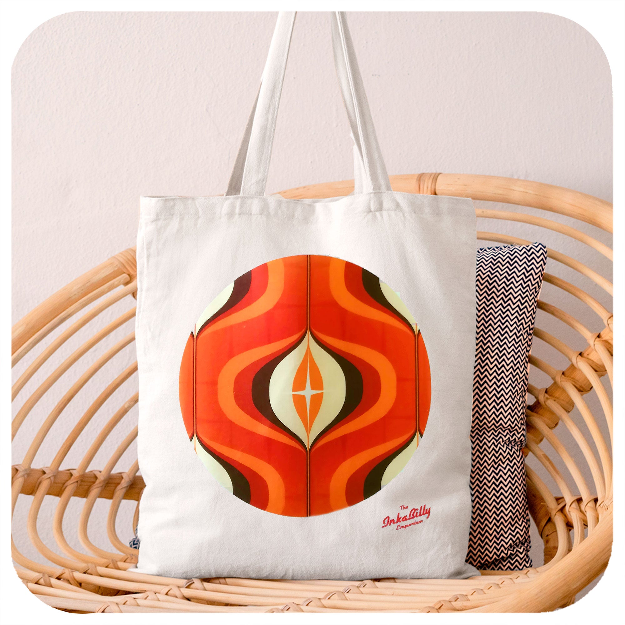 A white tote bag with orange 70s graphic design sits on a rattan chair | The Inkabilly Emporium