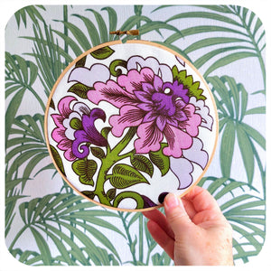 Embroidery hoop with floral design held against a tropical leaf patterned background