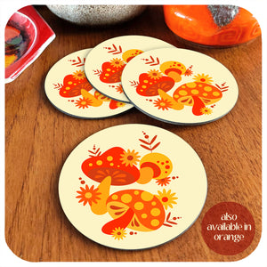 Set of 4 cream and orange 70s style coasters featuring 70s style mushrooms lie on a teak table with various vintage pottery pieces in the background. Text in the bottom righthand corner reads: also available in orange | The Inkabilly Emporium