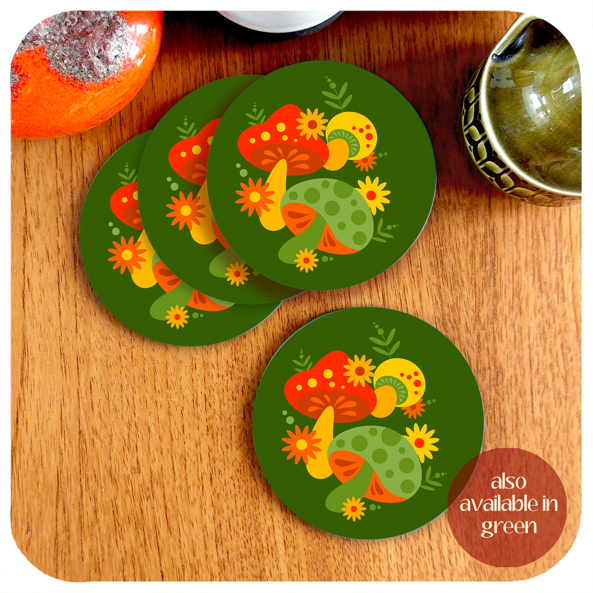 Set of four round 70s style mushroom coasters, in green, on a teak table surrounded by various vintage mid century pottery pieces. Text in corner reads: also available in green | The Inkabilly Emporium