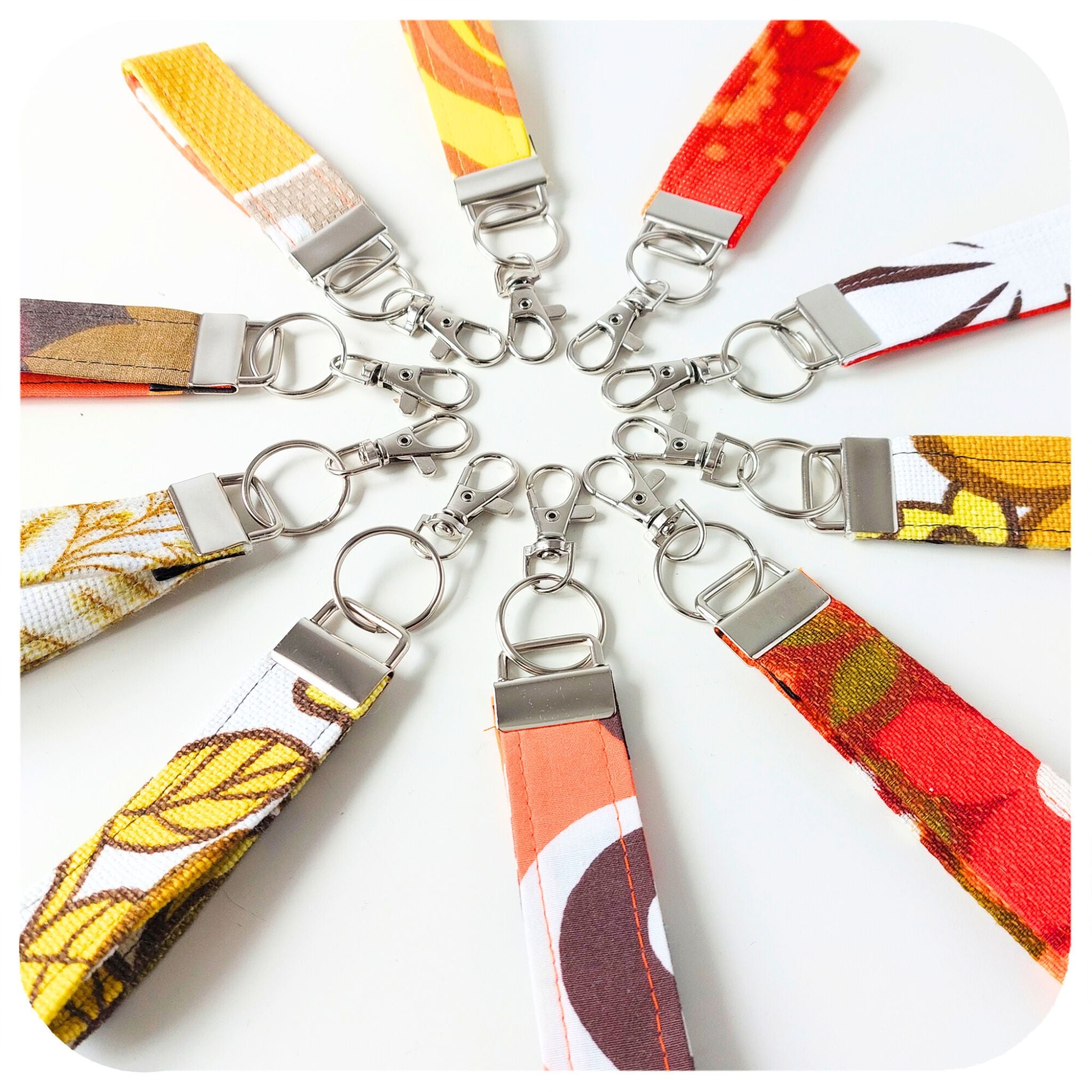 Colourful fabric keychains with metal clasps arranged in a circular pattern on a white background.