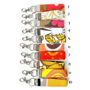 Colourful fabric keychains with metal clasps on a white background, with reference numbers