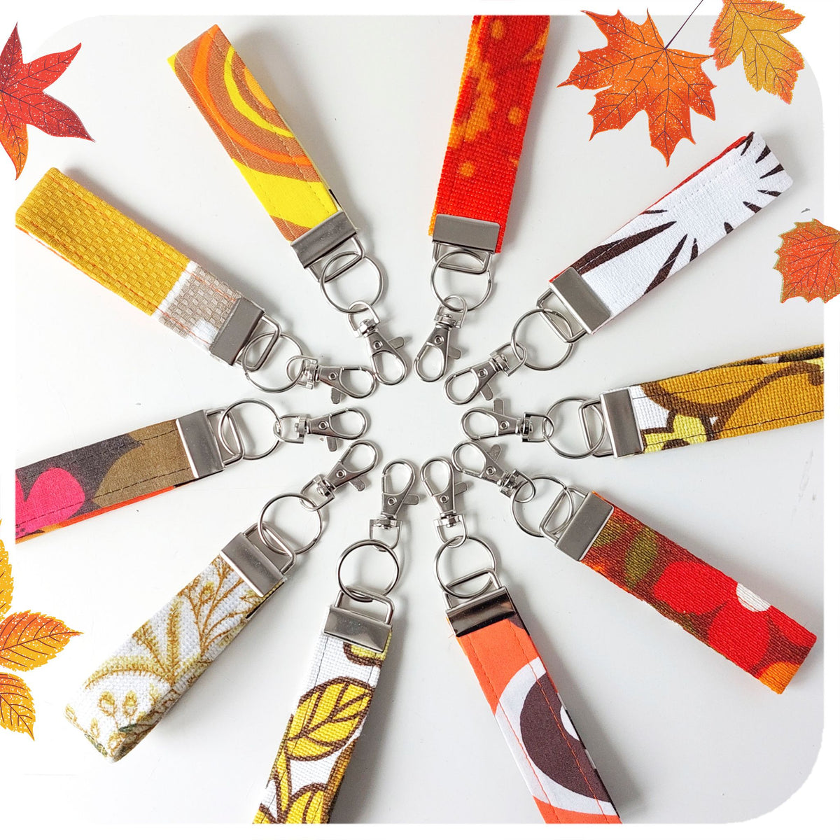 Colourful fabric keychains with metal clasps arranged in a circular pattern on a white background.