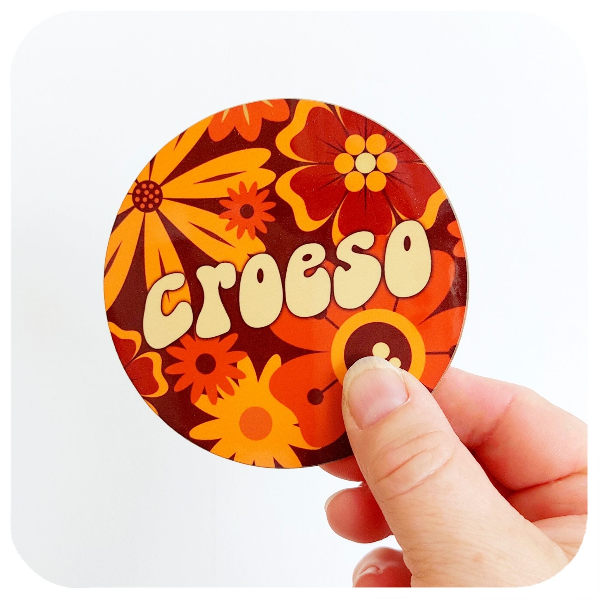 A coasters in a 70s floral design featuring the word Croeso, held against a white background | The Inkabilly Emporium