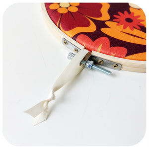 Floral-patterned embroidery hoop with a cream ribbon loop and metal clamp on a white background