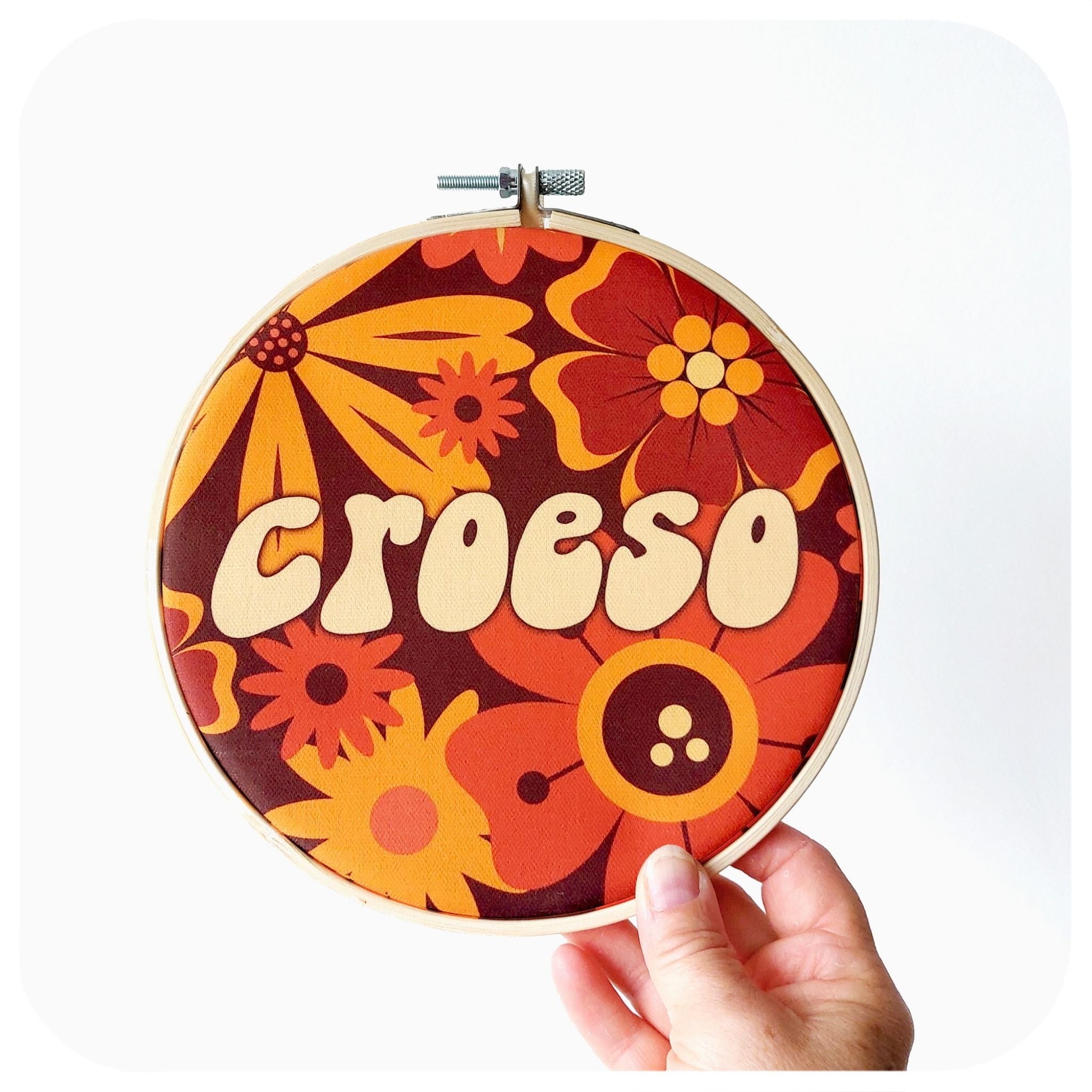 Decorative hoop with floral design and 'CROESO' text held by a hand on a white background