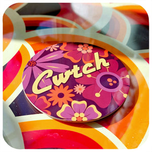 Colourful coaster with floral design and 'Cwtch' text on a 70s patterned table