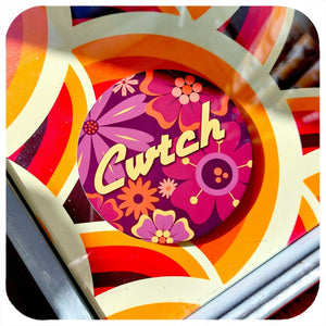 Colourful round coaster with floral elements and the word 'Cwtch' on a 70s style table