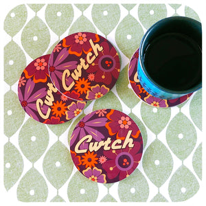 Floral coasters with 'Cwtch' text on a green patterned surface with a mug.