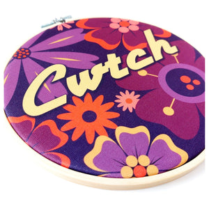 Decorative hoop with colorful floral pattern and 'Cwtch' text on a purple background