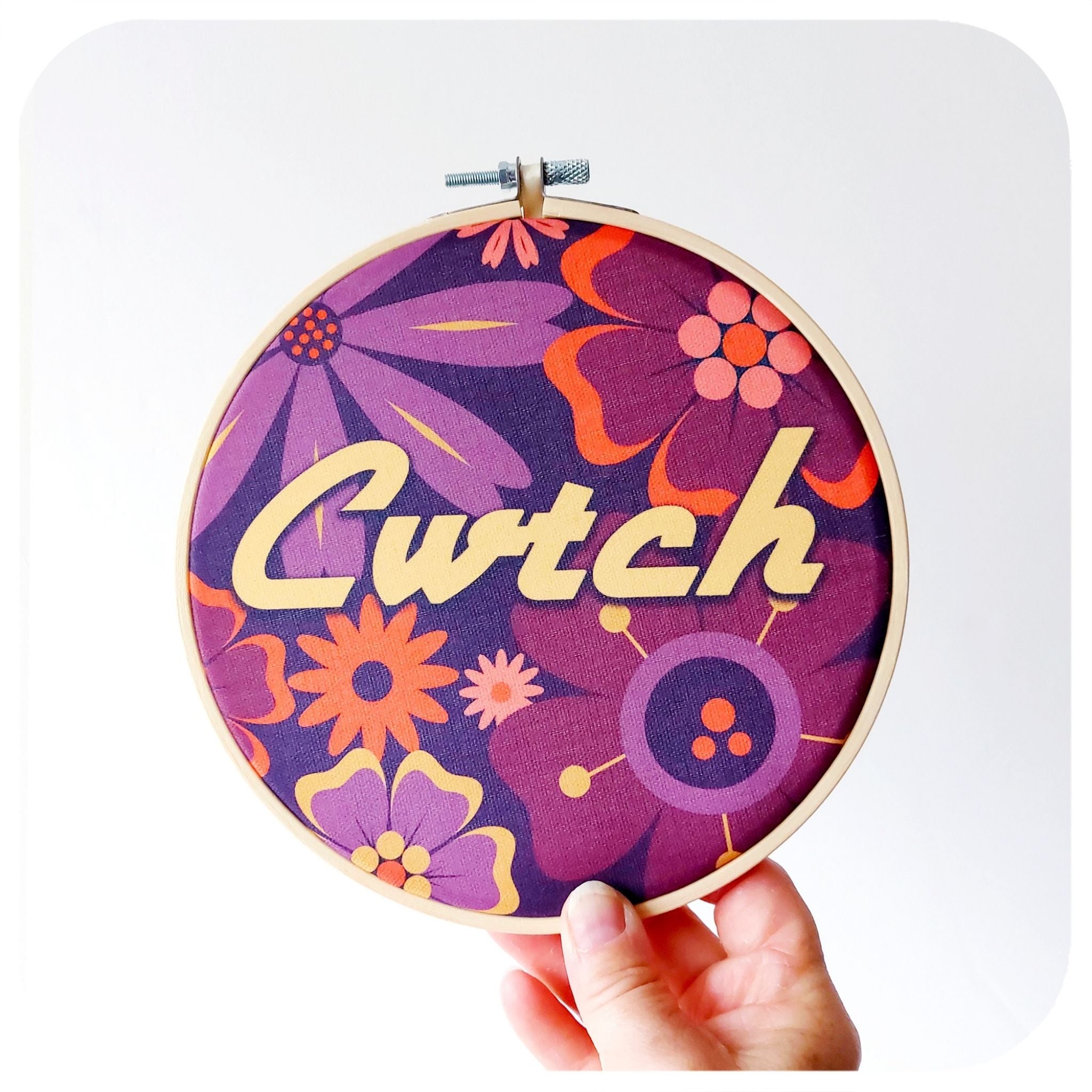 Decorative hoop with floral pattern and 'Cwtch' text held against a white background