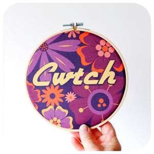 Decorative hoop with floral pattern and 'Cwtch' text held against a white background