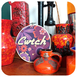 Collection of colourful ceramic vases and a decorative hoop with 'Cwtch' text on a wooden surface.