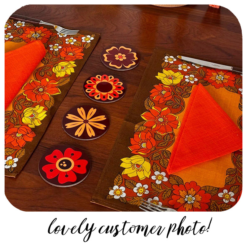 Floral table setting with placemats, coasters, and napkins on a wooden table.