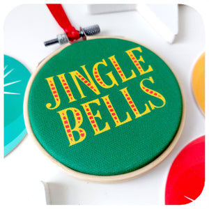 Close up of a retro style christmas tree decoration lies on a white background. Text on ornament reads; Jingle Bells | The Inkabilly Emporium