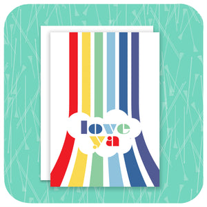 An A6 greetings card featuring a vertical rainbow with the words "Love Ya" sits on a white envelope  on a  textured light green background | The Inkabilly Emporium