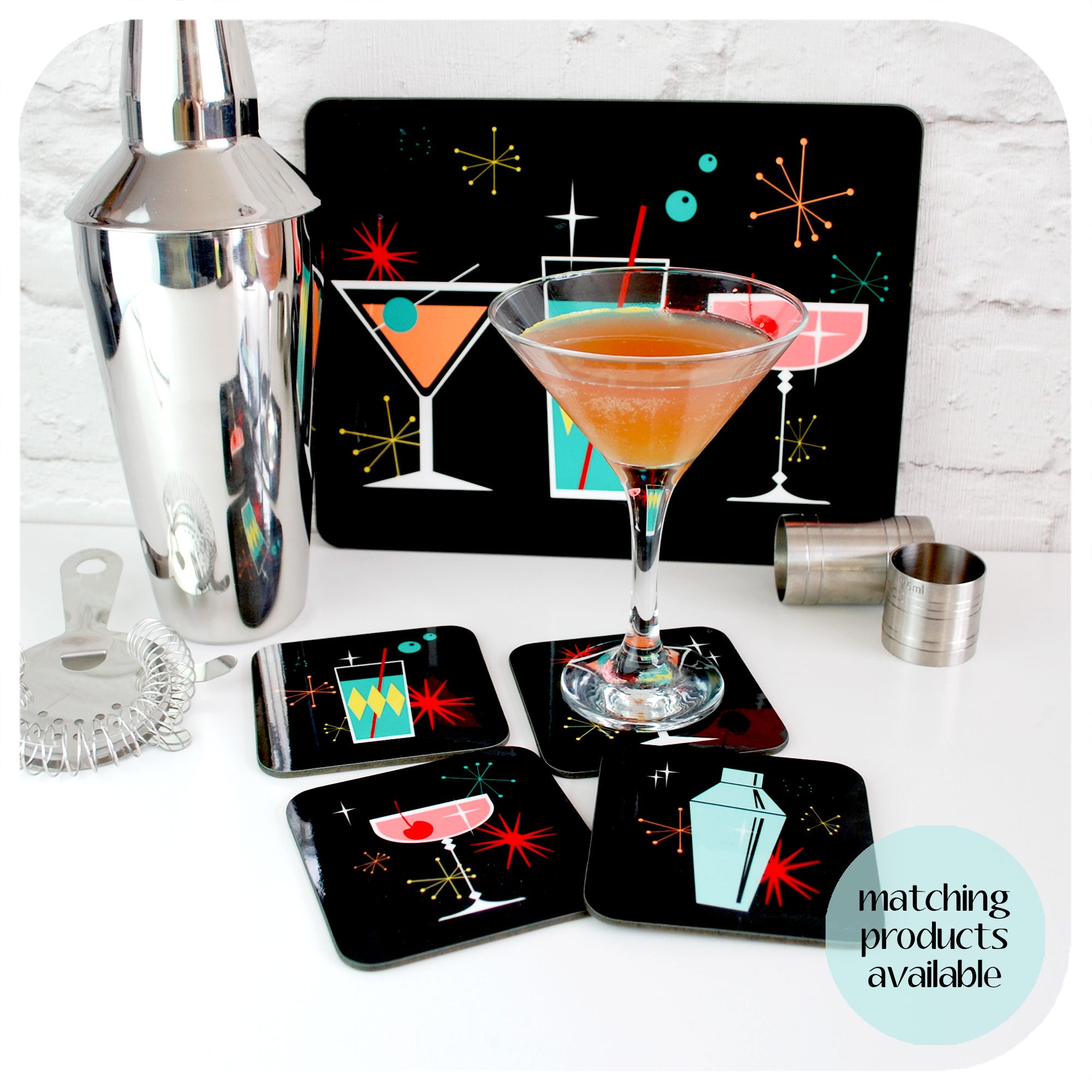 A retro cocktail shaker, bar accessories and a martini style cocktail sit with a set of retro cocktails coasters and a single placemat | The Inkabilly Emporium