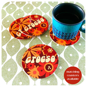 Colourful coasters with 'Croeso' text on a patterned surface with a blue mug.