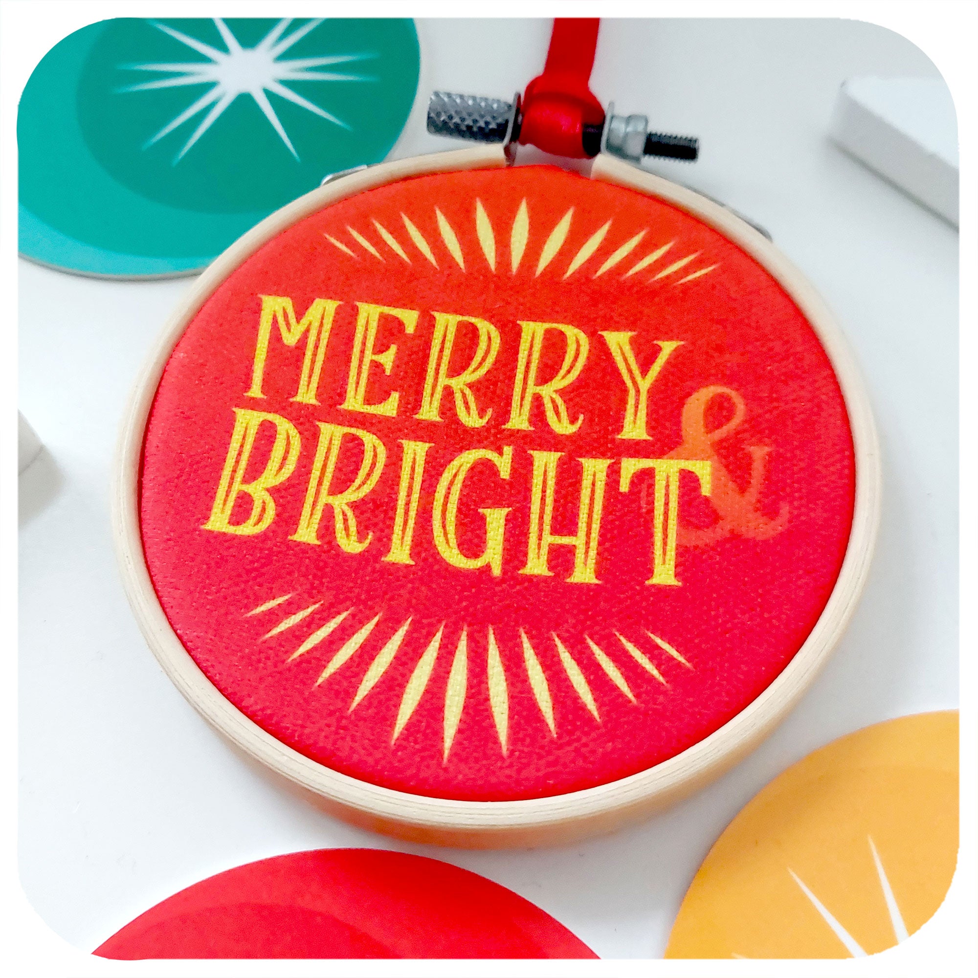 Close up of a retro style christmas tree decoration lies on a white background. Text on ornament reads; Merry & Bright
